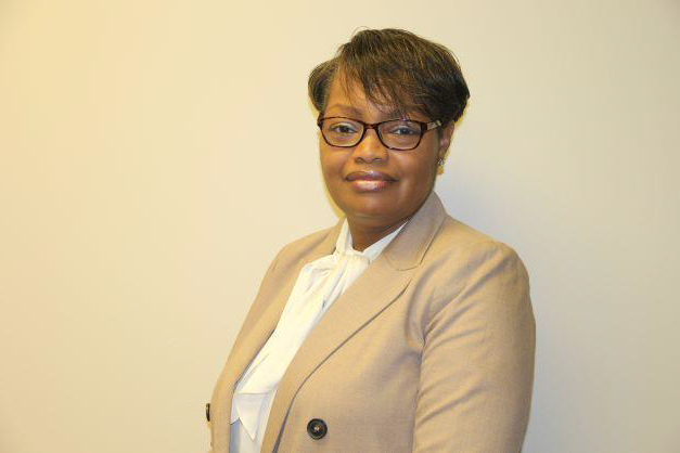 African American female wearing a black glasses, tan blazer with black button, and white shirt posing for a photo